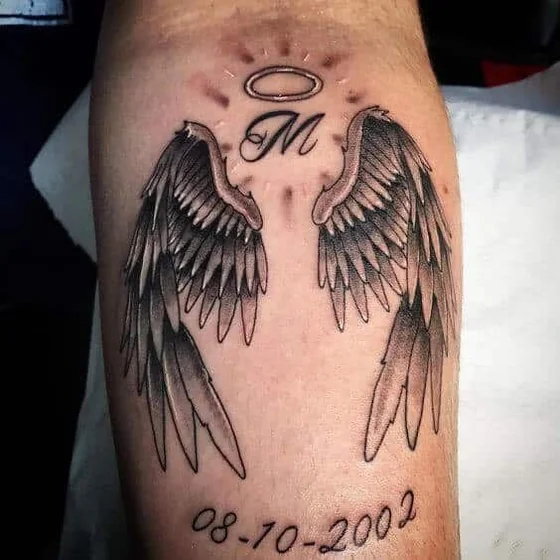 Black And Grey angel wing with initial and date tattoo idea for men on upper arm