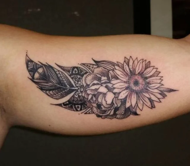 Black and grey floral feather tattoo idea for women on upper arm.