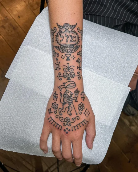 Blackwork linework angel, skull, lion, Hebrew text tattoo for women on forearm and hand.