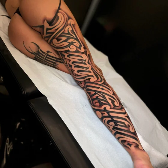 Blackwork ornamental script calligraphy tattoo for women on thigh and leg