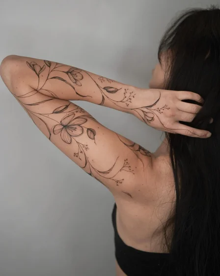 Delicate floral vine fine line tattoo for ladies on arm and forearm