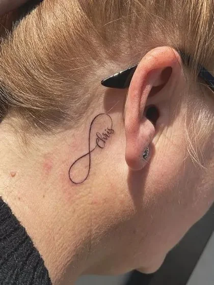 Fine Line Script Infinity Name tattoo design for women behind the ear