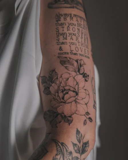 Fine Line flower and quote tattoo for women on upper arm.