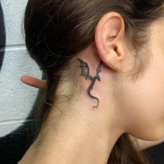 Fine line minimalist dragon tattoo idea for women behind the ear