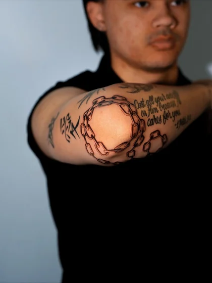 Men's linework chain and Bible verse script tattoo on elbow and forearm