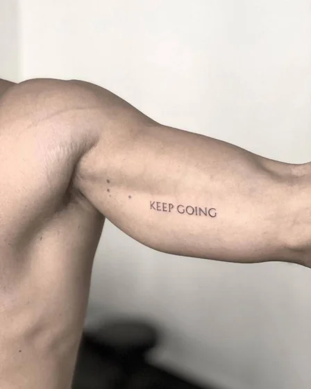 Minimalist 'Keep Going' quote tattoo idea for men on upper arm