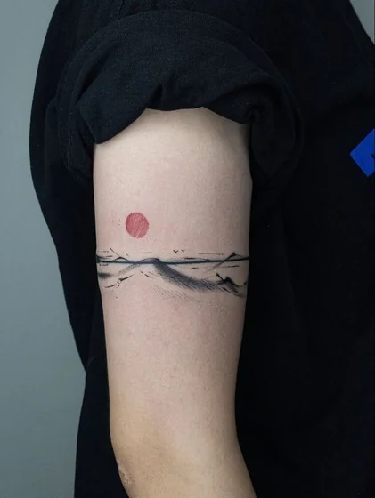 Minimalist Sumi-e sun and mountain tattoo idea for men and women on upper arm