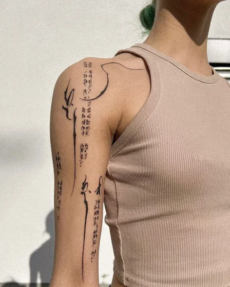 Minimalist abstract script tattoo idea for women on upper arm and shoulder