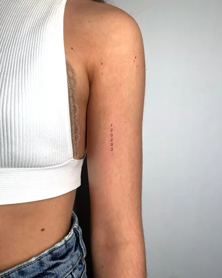Minimalist fine line numbers tattoo design for women on upper arm