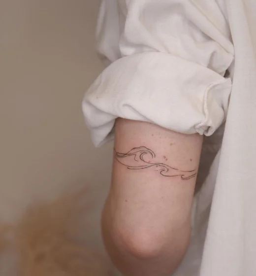 Minimalist fine line ocean waves arm band tattoo design for women on upper arm