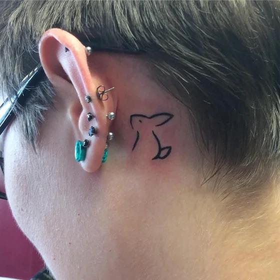 Minimalist fine line rabbit tattoo design for women behind the ear