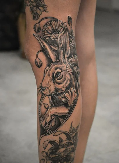 Realistic black and grey rabbit and floral tattoo idea for women on knee and calf