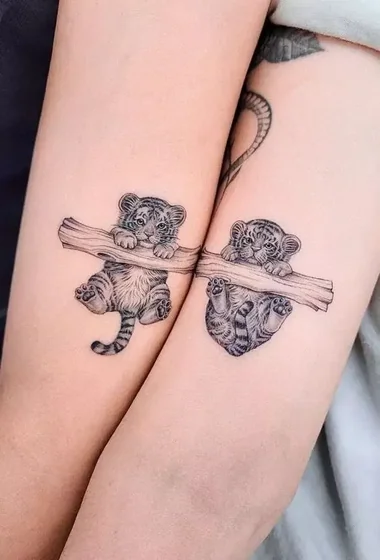 Realistic black and grey tiger cubs on a tree branch tattoo design for women on upper arm tattoo ideas
