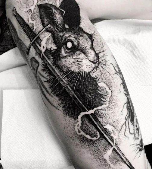 Realistic dotwork rabbit and sword tattoo design on upper arm