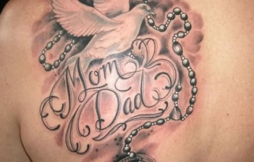 Realistic dove, rosary, and script 'Mom Dad' tattoo idea on back shoulder