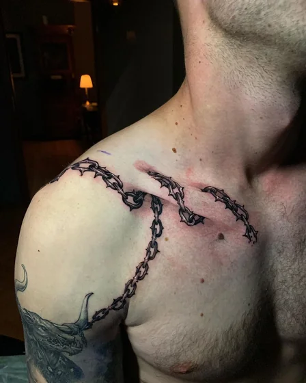 Realistic spiked chain and dragon tattoo for men on shoulder.