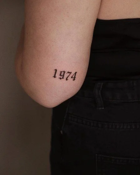 Script '1974' year tattoo idea for women on elbow