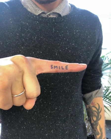 Script 'SMILE' word tattoo idea for men on finger and forearm