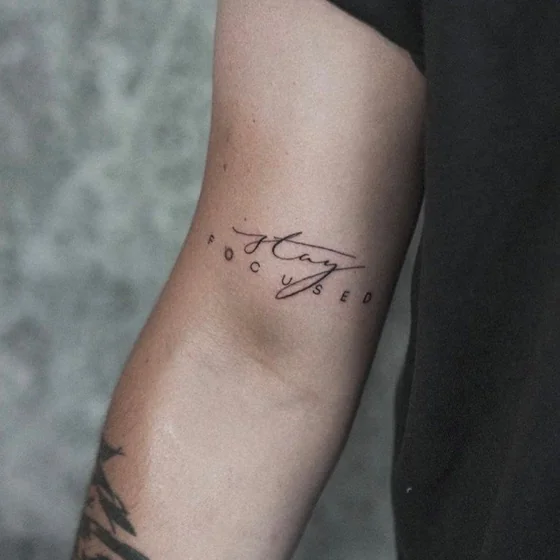 Script fine line 'Stay Focused' quote tattoo for men on upper arm