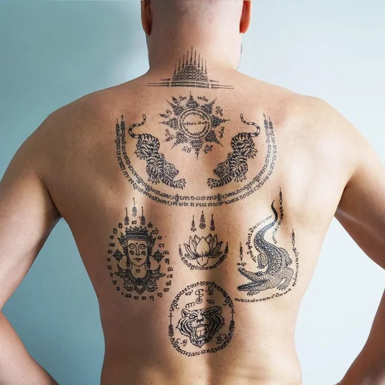 Traditional Sak Yant patchwork tattoo idea for men: tigers, lotus, crocodile, deity face on back.