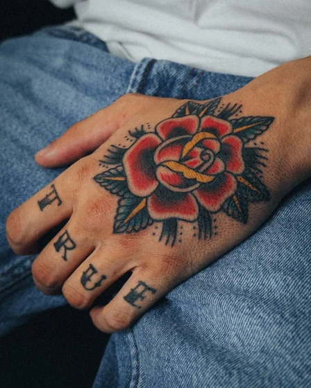 Traditional rose and word tattoo for men on hand and finger
