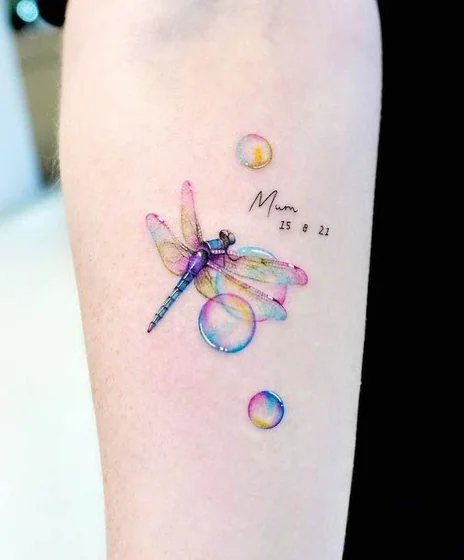 Watercolor dragonfly, word, and bubble tattoo design for women on forearm