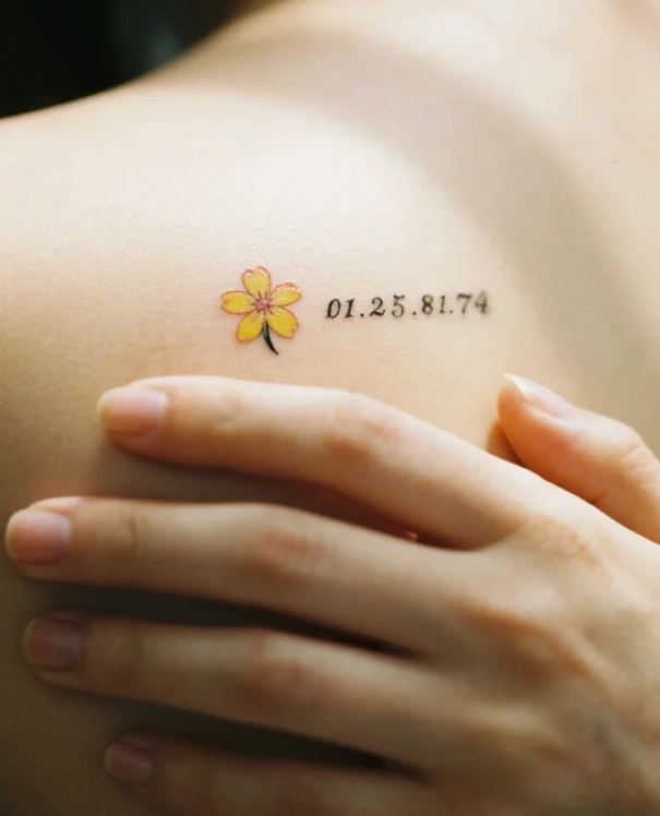 fine-line birth flower and tiny script coordinates tattoo near the collarbone as a subtle personal memory piece